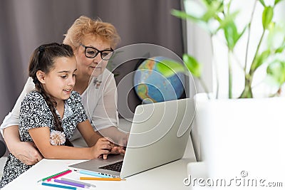 This is my favourite movie. Shot of an adorable little girl using a laptop while sitting at home with her grandmother. Stock Photo