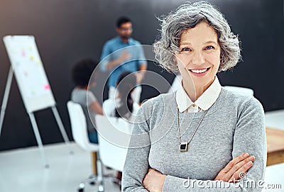 My teams got it covered. Portrait of a businesswoman standing with her arms folded in the boardroom while a colleague Stock Photo