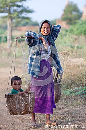 Burmese woman carrying baby and firewood in basket over fields i Editorial Stock Photo