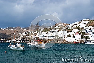 Mykonos, Greece - May 04, 2010: Fishing village at seaside on cloudy sky. Houses at sea coast. Boats in blue sea on Editorial Stock Photo