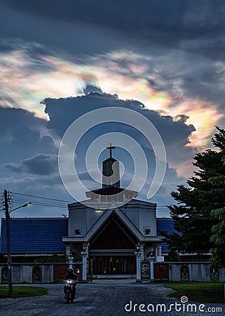 Mysterious cloud iridescence phenomenon glowing over christian church in the evening Stock Photo