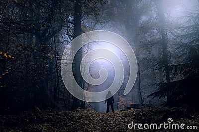 A mysterious concept edit. A lone figure standing on a forest path on a spooky misty night looking at lights in the sky. With a hi Stock Photo