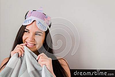 Mysterious cute young woman with long straight dark hair in sleeping eye mask with unicorn on grey background. Female sheltering Stock Photo