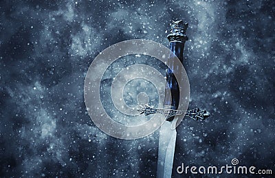 mysterious and magical photo of silver sword over gothic snowy black background. Medieval period concept. Stock Photo