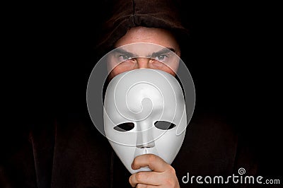 Mysterious man in black hiding his face behind white mask Stock Photo