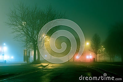 A mysterious moody street with trees silhouetted against street lights on a foggy atmospheric winters night Stock Photo