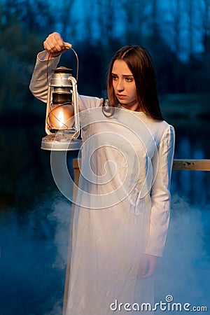 Mysterious mystical girl in a dark night forest with a kerosene lamp in her hands Stock Photo