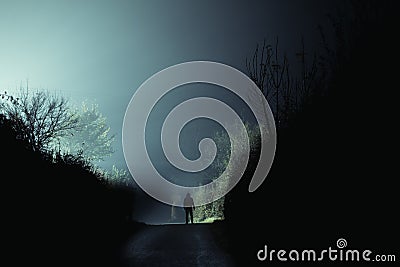 A mysterious scary hooded figure. Standing in the middle of the road. On a spooky, foggy winters night in the countryside Stock Photo