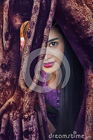 Mysterious woman,Beautiful woman with long dark hair and red lips resting in the tree roots and looking at you. Stock Photo