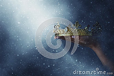 Mysteriousand magical image of woman`s hand holding a gold crown over gothic black background. Medieval period concept. Stock Photo