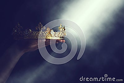 Mysteriousand magical image of woman`s hand holding a gold crown over gothic black background. Medieval period concept. Stock Photo