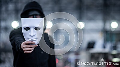 Mystery hoodie man with black mask holding white mask in his hand. Anonymous social masking or bipolar disorder concept Stock Photo