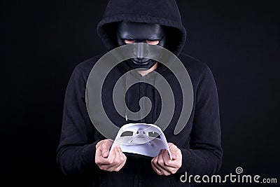 Mystery man holding and looking at white mask Stock Photo