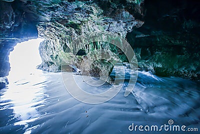 Mystic cave by the sea, view from inside the cave looking out, sunbeam shines down on ripple sand beach into the cave Stock Photo