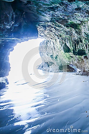 Mystic cave by the sea, view from inside the cave looking out, sunbeam shines down on ripple sand beach into the cave Stock Photo