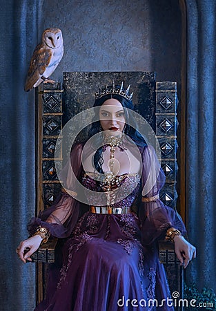 Mythical fantasy woman queen vamp sits on medieval ancient throne. Golden gothic crown on head. Elf girl princess evil Stock Photo