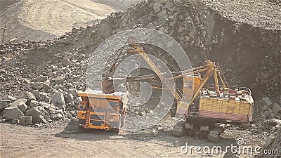 A máquina escavadora carrega o minério em um caminhão basculante, em uma máquina escavadora e em um caminhão basculante da minera video estoque A máquina escavadora carrega o minério em um caminhão basculante, em uma máquina escavadora e em um caminhão basculante da minera video estoque