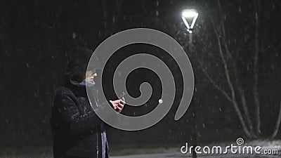 Mężczyzna w latarni ulicznej Facetów spojrzenia w jego smartphone Ja ` s snowing przeciw tłu lampa swobodny ruch zbiory Mężczyzna w latarni ulicznej Facetów spojrzenia w jego smartphone Ja ` s snowing przeciw tłu lampa swobodny ruch zbiory