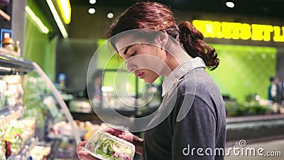 Młoda piękna brunetki dziewczyna próbuje wybierać w jej 20 s ` prepacked sałatkowych liście w sklepie spożywczym Młoda piękna brunetki dziewczyna próbuje wybierać w jej 20 s ` prepacked sałatkowych liście w sklepie spożywczym