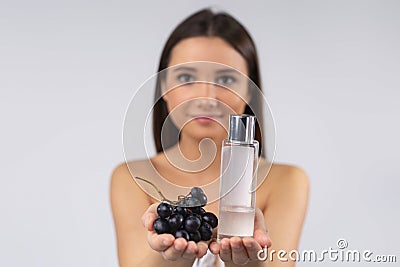 Selective focus. Naked brunette with fresh grape and grape seed oil in bottle. Skin care cosmetic product for poster Stock Photo