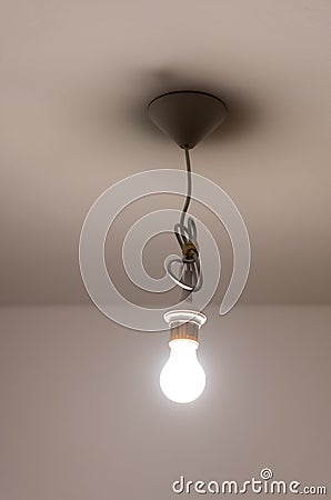 Naked lit light bulb hanging from the ceiling of a dimly lit room Stock Photo