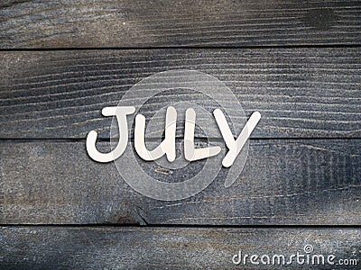 The name of the month is composed of light wooden letters on dark wood. The month of July. Stock Photo