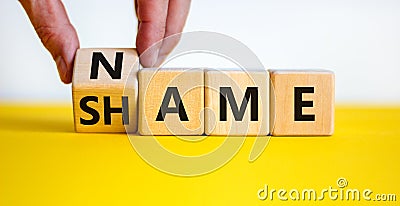 Name or shame symbol. Businessman turns the wooden cube and changes the word `shame` to `name` or vice versa. Beautiful yellow Stock Photo