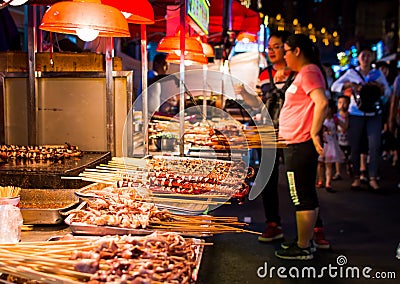 NANNING, CHINA - JUNE 9, 2017: Food on the Zhongshan Snack Street, a food market in Nanning with many people bying food and Editorial Stock Photo