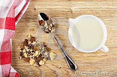 Napkin, heap of muesli, granola with banana and chocolate in spoon, pitcher with yogurt on table. Top view Stock Photo