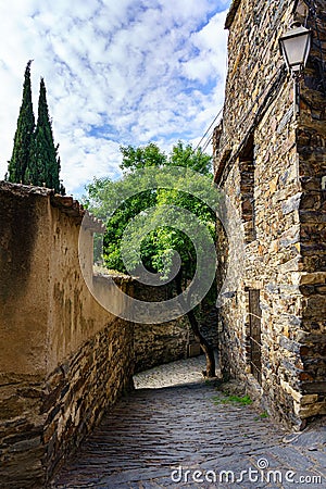 Narrow alley with old stone houses and blue sky with clouds, cypress trees and stray cat. Patones de Arriba Madrid Stock Photo