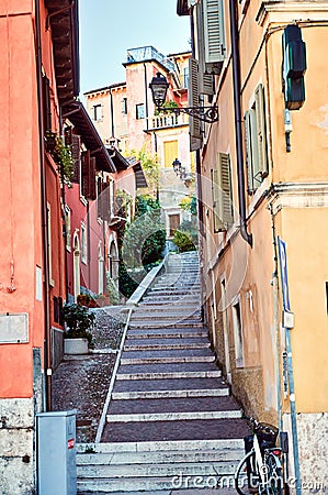 Narrow ancient street flowers sidewalk stone steps colorful facade Italy center Verona Stock Photo