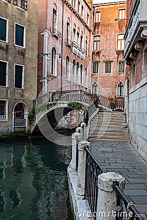 Narrow canal with medieval buildings, stone walkway in Venice, Italy on sunny day Editorial Stock Photo