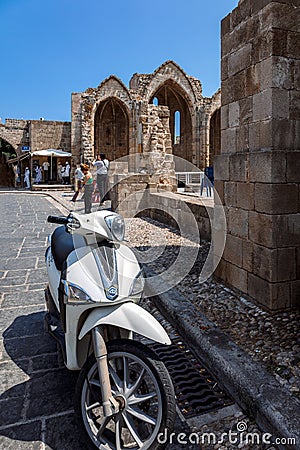 Narrow cobbled historical streets of Rhodes. Tourists walk on Old Town. Vintage scooter bike is parked old stone against Editorial Stock Photo