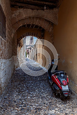 Narrow cobbled historical streets of Rhodes. Vintage scooter bike is parked old stone against wall of house, Rhodes Stock Photo