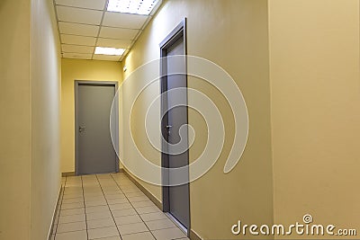 A narrow light corridor in the office room with a few gray doors Stock Photo