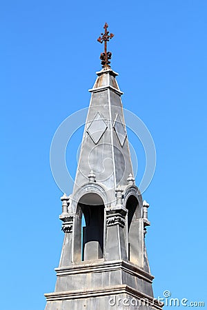 Narrow light grey metal gothic church tower with various decorative elements and rusted cross on top Stock Photo