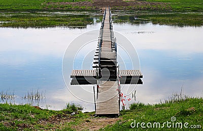 Narrow pedestrian wooden bridge on smooth water across a wide river Stock Photo