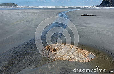 Small stream flowing past exposed stone on deserted unspoiled beach Stock Photo