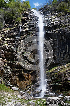 Narrow white stream of water flows over a wet stone cliff Stock Photo