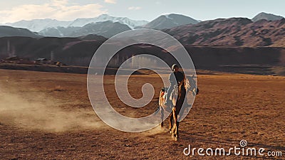 Naryn, Kirgizstan - April 4, 2019: A young boy rides a horse through a valley against the mountains. An aerial dynamic Editorial Stock Photo