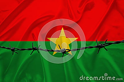 National flag of Burkina Faso on satin, iron barbed wire, concept of war, revolution, an armed uprising in the country, shootout Stock Photo