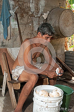 Native senior man cleaning slicing fresh coconut for production Stock Photo