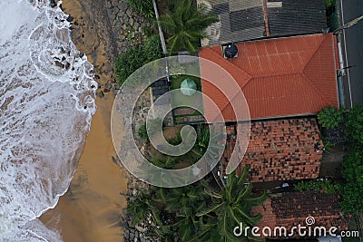 Natural aerial drone bird view day shot of the sea shore with beautiful villas, green trees, yellow sand and big white waves and Stock Photo