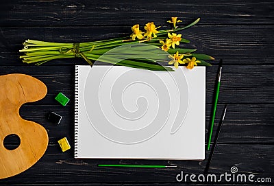 Sketchbook, watercolor and brushes on black wooden table with bouquet of daffodils. Flat lay, top view Stock Photo
