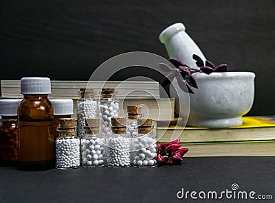 Natural Homeopathy Concept â€“ Healing herbs in a mortar and pestle next to homeopathic medicine consisting a bottle of pills- Stock Photo