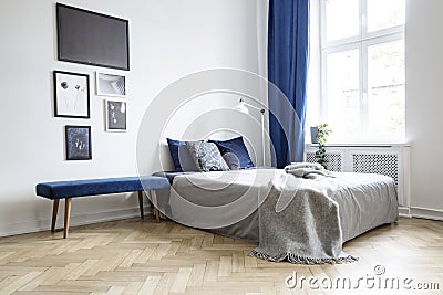 Natural light coming through a large window into a white and navy blue bedroom interior with cozy bed and wooden floor Stock Photo