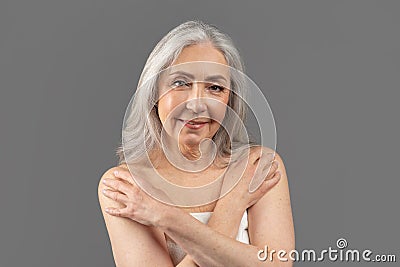 Natural mature beauty. Charming senior woman in towel having smooth skin after shower, posing on grey background Stock Photo