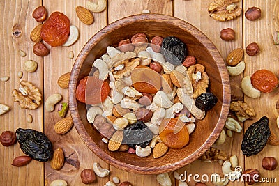 Natural nutritious mix of different nuts with dried apricots and plums in a wooden round plate on the brown wooden table. Mixture Stock Photo