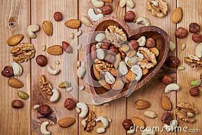 Natural nutritious mix of different nuts in a wooden plate of heart symbol shape on brown wooden table. Mixture of walnuts, huzeln Stock Photo