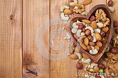 Natural nutritious mix of different nuts in a wooden plate of heart symbol shape on brown wooden table at the right side. Mixture Stock Photo